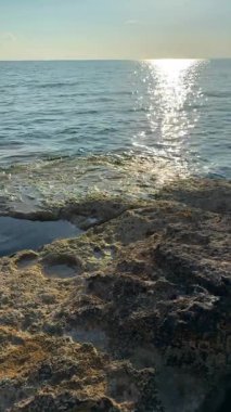 Güneş ışığı altında parıldayan sığ kıyı suları Kuzey Kıbrıs 'taki kayalık sahildeki kayaları ortaya çıkarıyor. Doğal güzellik, sükunet ve deniz suyunun dinamik hareketi kavramı. Dikey