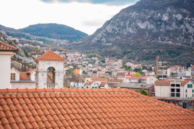 Karadağ 'ın Kotor kentinde terracotta çatısı olan tarihi çan kulesi dramatik bir dağ manzarasına karşı duruyor. Ortaçağ mimarisi, Adriyatik mirası ve manzaralı eski kasaba cazibesi kavramı. 