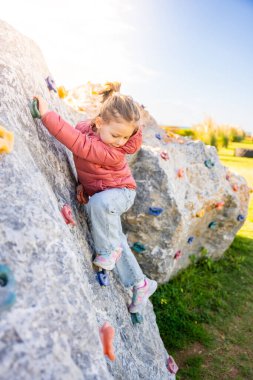 Oyun parkında yapay bir tırmanma duvarına tırmanan küçük bir kız güç ve koordinasyon geliştiriyor. Yüksek kalite fotoğraf