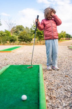 Küçük kız dışarıda mini golf oynuyor. Çocuk bahar zamanı yeni aktivitelerle eğleniyor. Aile tatilleri ya da tatil köyleri. Yüksek kalite fotoğraf