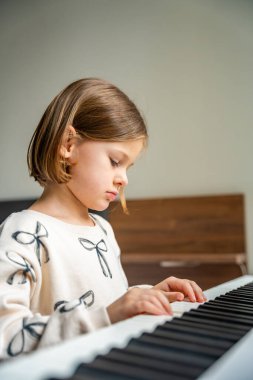 Beyaz piyano sentezleyicili kız için ev müziği dersi. Erken gelişim kavramı: müzik öğrenmek motor becerileri, işitme ve zekayı geliştirir, çocukluktan itibaren yaratıcılığı teşvik eder.. 