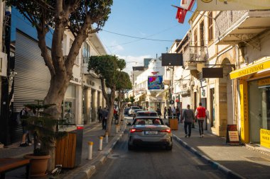 Girne, Kuzey Kıbrıs - 3 Şubat 2025: Kyrenia şehir merkezinde yayalar, arabalar, kafeler, dükkanlar ve yürüyen turistlerle dolu bir sokak, Kuzey Kıbrıs. Yüksek kalite fotoğraf