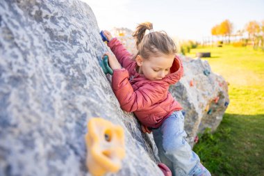 Oyun parkında yapay bir tırmanma duvarına tırmanan küçük bir kız güç ve koordinasyon geliştiriyor. Yüksek kalite fotoğraf