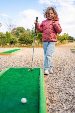 Küçük kız dışarıda mini golf oynuyor. Çocuk bahar zamanı yeni aktivitelerle eğleniyor. Aile tatilleri ya da tatil köyleri. Yüksek kalite fotoğraf
