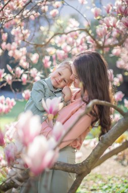 Prag parkındaki manolya ağaçlarının altında küçük kızıyla modaya uyan bir anne. Modern bir ebeveynlik yaklaşımıyla şık bir aile anı yakalamak. Yüksek kalite fotoğraf