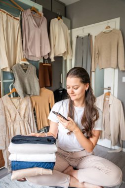 Genç bir kadın, akıllı telefonuyla gardıropta asılı kıyafetleri fotoğraflıyor. Çevrimiçi satış ve ikinci el moda mobil uygulamalar sayesinde gelişiyor, sürdürülebilir alışverişi daha ulaşılabilir hale getiriyor.