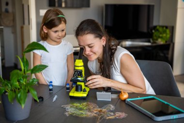 Küçük kız ve annesi evde mikroskop altında soğan derisini inceliyor. Aile bilimi eğitimi ve erken biyoloji eğitimi kavramı. Yüksek kalite fotoğraf
