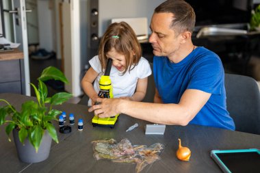 Baba ve kızı evdeki mikroskop altında çeşitli bitki örneklerini inceliyor. Aile bilimi eğitimi ve botanik araştırması kavramı. Yüksek kalite fotoğraf