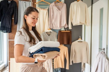 Genç bir kadın elinde bir yığın kıyafet tutuyor. Satmak, bağışlamak ya da geri dönüşüm için eşyalar ayırıyor. Sürdürülebilir moda ve ikinci el kullanımı atıkları azaltmaya ve bilinçli tüketimi teşvik etmeye yardımcı olur. 