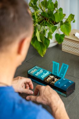 Adam haftalık ilaç organizatöründen ilaç ve takviye alıyor. Günlük ilaç alımı ve sağlık rutini kavramı. Yüksek kalite fotoğraf