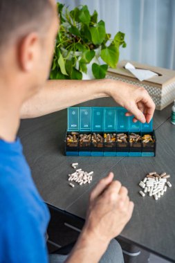 Haplarını ve takviyelerini haftalık ilaç organizatörüne ayıran bir adam. İlaç yönetimi ve günlük sağlık rutini kavramı. Yüksek kalite fotoğraf