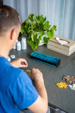 Haplarını ve takviyelerini haftalık ilaç organizatörüne ayıran bir adam. İlaç yönetimi ve günlük sağlık rutini kavramı. Yüksek kalite fotoğraf