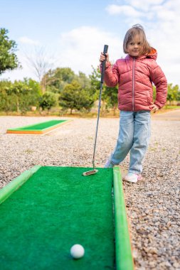Küçük kız dışarıda mini golf oynuyor. Çocuk bahar zamanı yeni aktivitelerle eğleniyor. Aile tatilleri ya da tatil köyleri. Yüksek kalite fotoğraf
