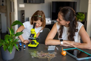 Anne ve kızı evdeki mikroskop altında çeşitli bitki örneklerini inceliyor. Aile bilimi eğitimi ve botanik araştırması kavramı. Yüksek kalite fotoğraf