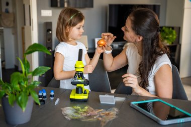 Küçük kız ve annesi evde mikroskop altında soğan derisini inceliyor. Aile bilimi eğitimi ve erken biyoloji eğitimi kavramı. Yüksek kalite fotoğraf