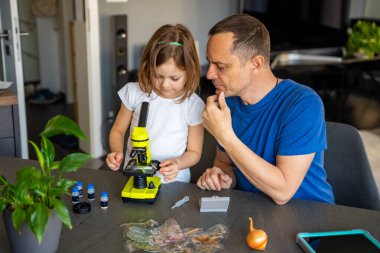 Baba ve kızı evdeki mikroskop altında çeşitli bitki örneklerini inceliyor. Aile bilimi eğitimi ve botanik araştırması kavramı. Yüksek kalite fotoğraf