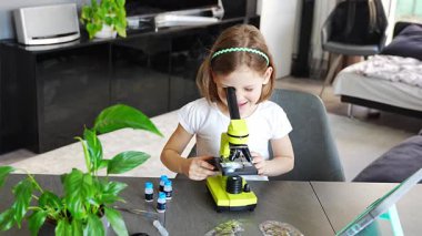 Küçük kız yeşil bir mikroskoptan bakıyor. Merakın ve erken bilimsel keşiflerin kavramı. Yüksek kalite 4k görüntü