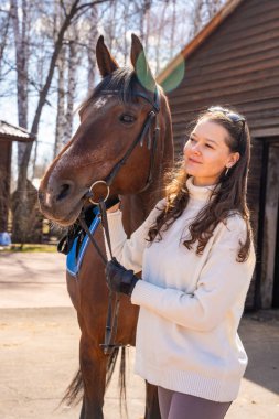 Ahırda atın yanında duran genç bir kadın. İnsanlar ve hayvanlar arasındaki duygusal bağ kavramı. Yüksek kalite fotoğraf
