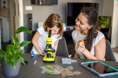 Küçük kız ve annesi evde mikroskop altında soğan derisini inceliyor. Aile bilimi eğitimi ve erken biyoloji eğitimi kavramı. Yüksek kalite fotoğraf