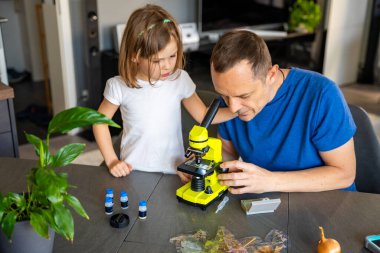 Baba ve kızı evdeki mikroskop altında çeşitli bitki örneklerini inceliyor. Aile bilimi eğitimi ve botanik araştırması kavramı. Yüksek kalite fotoğraf