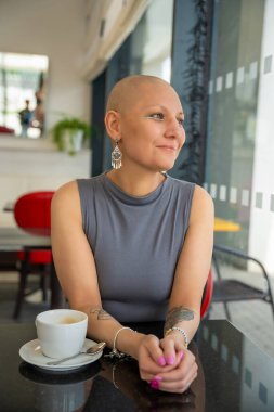 Kanserli, kendine güvenen, kafede kahve içen, hastalığa rağmen hayatı kucaklayan genç bir kadın. Konsept gösteriyor ki kanser teşhisi normal aktivitelerden zevk alma yeteneğini ortadan kaldırmıyor.. 