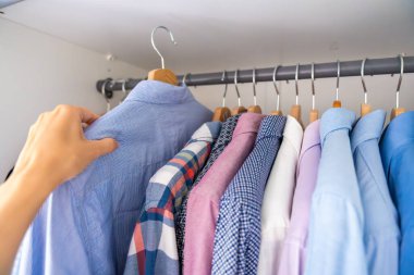 Erkek işçi, ahşap askılarda giysi dolu bir dolaptan gömlek seçiyor. Kıyafet seçimi kavramı, günlük rutin ve kişisel stil. Yüksek kalite fotoğraf