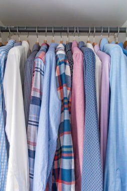 Gardıroptaki ahşap askılara asılmış erkek gömlekleri. Minimalist giyim organizasyonu ve klasik erkek moda konsepti. Yüksek kalite fotoğraf