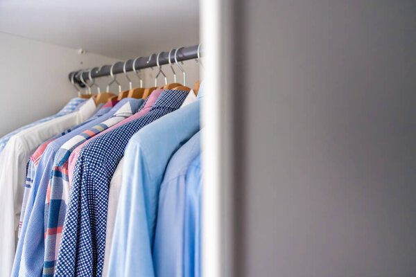 Мужские рубашки на деревянных вешалках частично видны за дверью шкафа. Концепция повседневного выбора одежды и организованное пространство мужского гардероба. Высокое качество фото