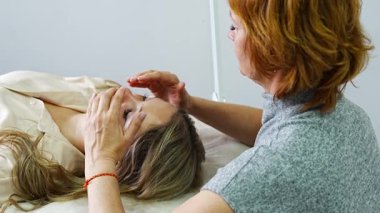 Kadın pratisyen, kanepede uzanan genç bir kadına yüz gerdirme tekniği uyguluyor. Enerji iyileştirme kavramı, yüz terapisi ve Erişim Çubukları 'ndan alternatif sağlık uygulaması. Yüksek kalite 4k görüntü