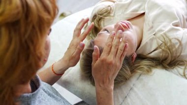 Kadın pratisyen, kanepede uzanan genç bir kadına yüz gerdirme tekniği uyguluyor. Enerji iyileştirme kavramı, yüz terapisi ve Erişim Çubukları 'ndan alternatif sağlık uygulaması. Yüksek kalite 4k görüntü