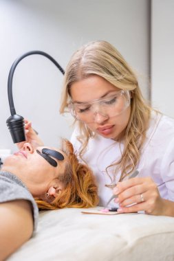 Modern güzellik salonunda ultraviyole lamba kullanarak kirpik uzatma işlemi. Kusursuz uygulama teknikli yenilikçi kırbaç geliştirme teknolojisi. Yüksek kalite fotoğraf