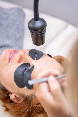 Güzellik uzmanı morötesi lambayla kirpik uzatma işleminden önce mor göz bandı uyguluyor. Modern güzellik salonunda yenilikçi kirpik uzatma metodu. Yüksek kalite fotoğraf