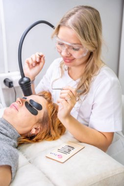 Modern güzellik salonunda ultraviyole lamba kullanarak kirpik uzatma işlemi. Kusursuz uygulama teknikli yenilikçi kırbaç geliştirme teknolojisi. Yüksek kalite fotoğraf