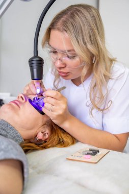 Modern güzellik salonunda ultraviyole lamba kullanarak kirpik uzatma işlemi. Kusursuz uygulama teknikli yenilikçi kırbaç geliştirme teknolojisi. Yüksek kalite fotoğraf