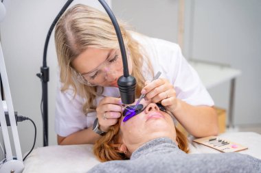 Modern güzellik salonunda ultraviyole lamba kullanarak kirpik uzatma işlemi. Kusursuz uygulama teknikli yenilikçi kırbaç geliştirme teknolojisi. Yüksek kalite fotoğraf