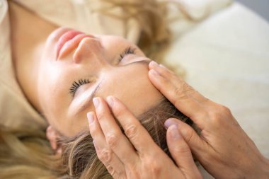 Erişim Çubuğu yüz gerdirme seansı sırasında genç bir kadının yüzüne yerleştirilmiş bir kadın pratisyenin elleri. Enerji işi kavramı, iyileştirme dokunuşu ve alternatif yüz terapisi. Yüksek kalite fotoğraf