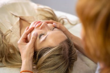 Erişim Çubuğu yüz gerdirme seansı sırasında genç bir kadının yüzüne yerleştirilmiş bir kadın pratisyenin elleri. Enerji işi kavramı, iyileştirme dokunuşu ve alternatif yüz terapisi. Yüksek kalite fotoğraf