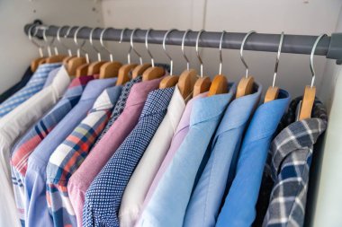 Gardıroptaki ahşap askılara asılmış erkek gömlekleri. Minimalist giyim organizasyonu ve klasik erkek moda konsepti. Yüksek kalite fotoğraf