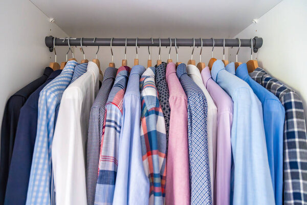 Аккуратно расставленные мужские рубашки, висящие на деревянных вешалках в шкафу. Минималистская организация одежды и классическая мужская концепция моды. Высокое качество фото