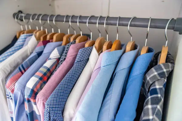 Gardıroptaki ahşap askılara asılmış erkek gömlekleri. Minimalist giyim organizasyonu ve klasik erkek moda konsepti. Yüksek kalite fotoğraf