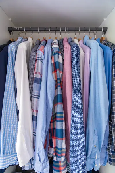 Gardıroptaki ahşap askılara asılmış erkek gömlekleri. Minimalist giyim organizasyonu ve klasik erkek moda konsepti. Yüksek kalite fotoğraf