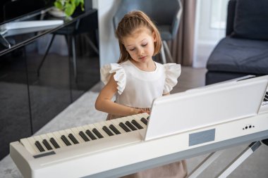 Evde, oturma odasında piyano çalan küçük bir kız. Çocukluk yaratıcılığı ve konforlu aile ortamında müzik gelişimi. Yüksek kalite fotoğraf