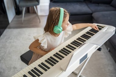 Evde kablosuz kulaklıkla piyano çalışan küçük bir kız. Modern ve odaklanmış müzik eğitimi yoluyla erken çocukluk gelişimi. Yüksek kalite fotoğraf