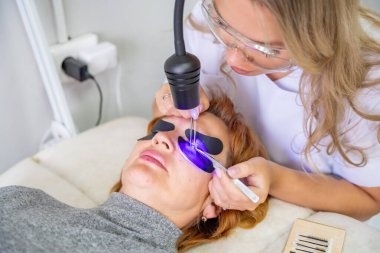 Modern güzellik salonunda ultraviyole lamba kullanarak kirpik uzatma işlemi. Kusursuz uygulama teknikli yenilikçi kırbaç geliştirme teknolojisi. Yüksek kalite fotoğraf