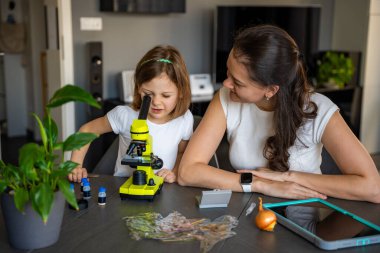 Küçük kız ve annesi evde mikroskop altında soğan derisini inceliyor. Aile bilimi eğitimi ve erken biyoloji eğitimi kavramı. Yüksek kalite fotoğraf