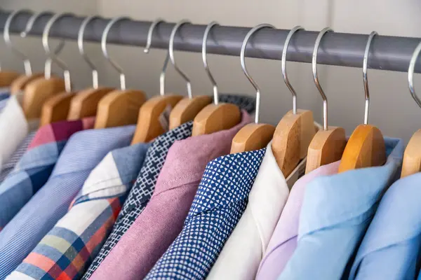 Gardıroptaki ahşap askılara asılmış erkek gömlekleri. Minimalist giyim organizasyonu ve klasik erkek moda konsepti. Yüksek kalite fotoğraf