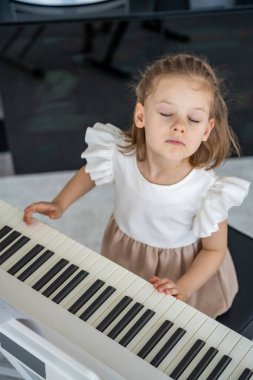 Küçük kız evde piyano çalarak eğleniyor. Neşeli bir müzikal ifade ve aile ortamında sesle duygusal bir bağ. Yüksek kalite fotoğraf