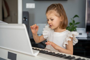 Evde, oturma odasında piyano çalan küçük bir kız. Çocukluk yaratıcılığı ve konforlu aile ortamında müzik gelişimi. Yüksek kalite fotoğraf