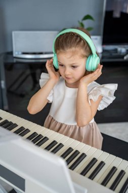 Evde kablosuz kulaklıkla piyano çalışan küçük bir kız. Modern ve odaklanmış müzik eğitimi yoluyla erken çocukluk gelişimi. Yüksek kalite fotoğraf