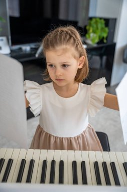 Evde piyano çalışmasından önce nota okuyan küçük bir kız. Konforlu bir aile ortamında müzikal öğrenme ve hazırlık odaklı bir an. Yüksek kalite fotoğraf